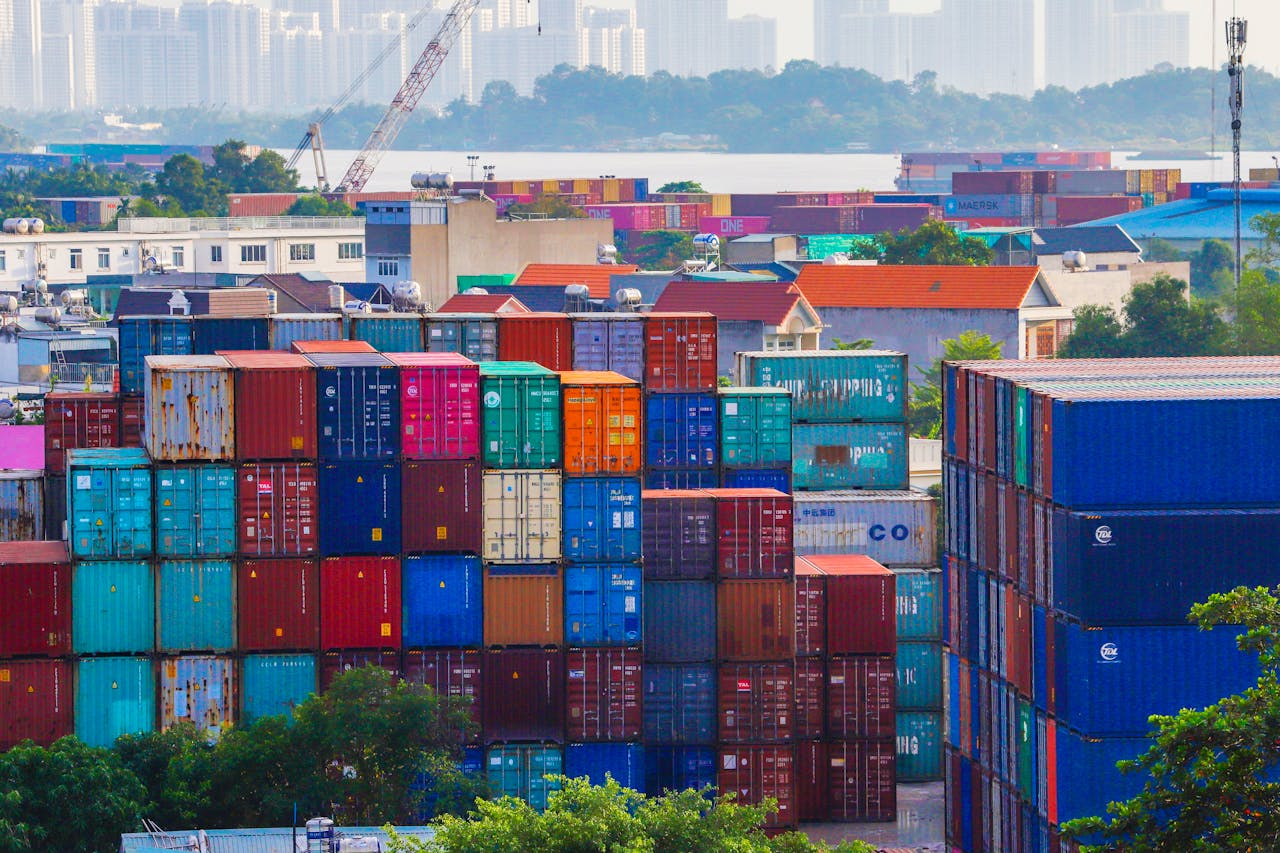 Vibrant stacked cargo containers at a bustling port with urban skyline in background.
