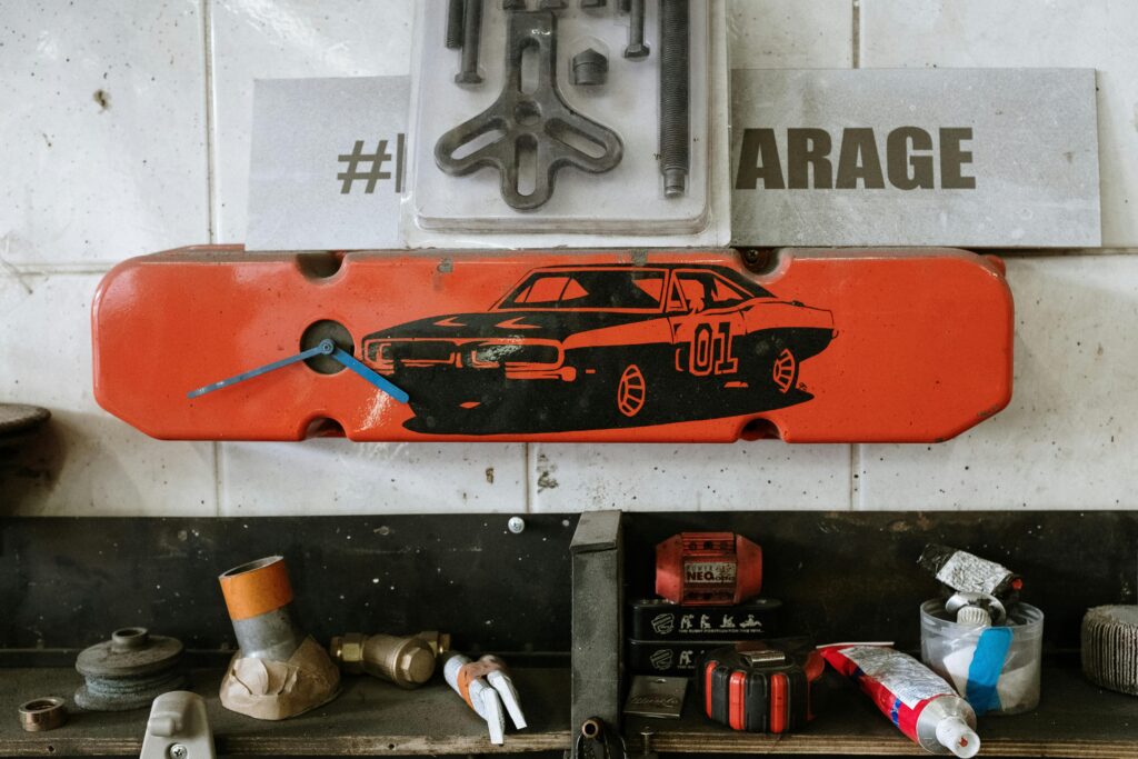 Red car part with a clock on a garage wall, surrounded by tools and auto parts.